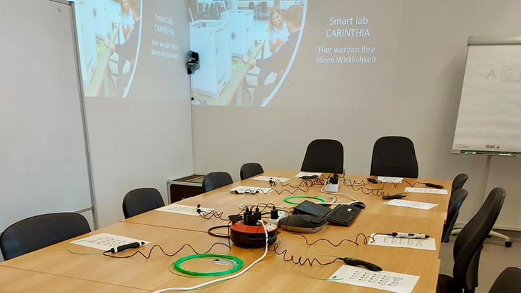 Konferenzraum mit schwarzen Stühlen, am Tisch Unterlagen und Kabel, an die Wand Präsentation mit Smart Lab Carinthia projiziert