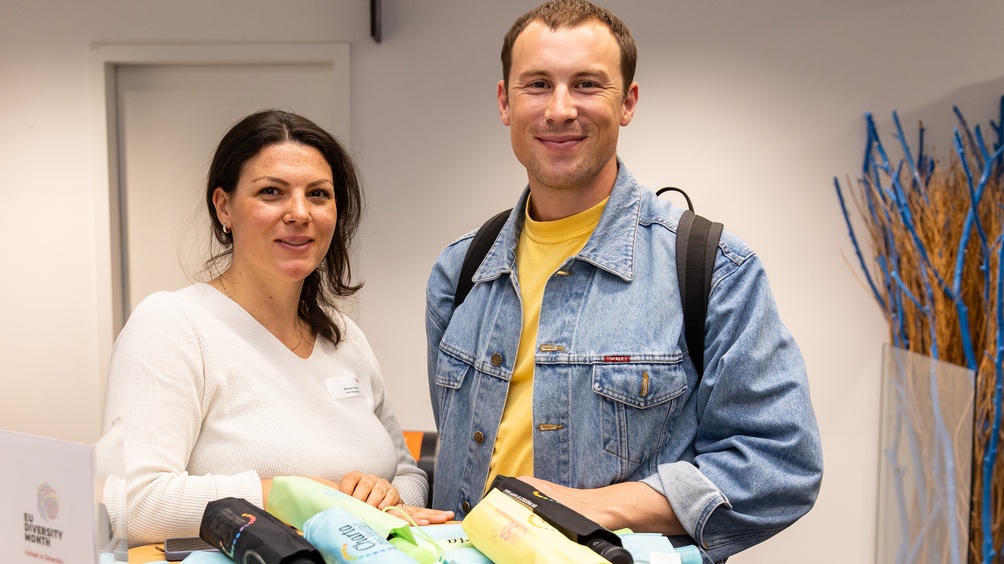 Zwei Personen im Gespräch miteinander, im Hintergrund verschwommen weitere Person