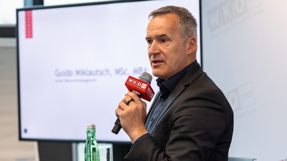 Porträt einer Person in leicht seitlicher Ansicht, die in ein Mikrofon spricht 