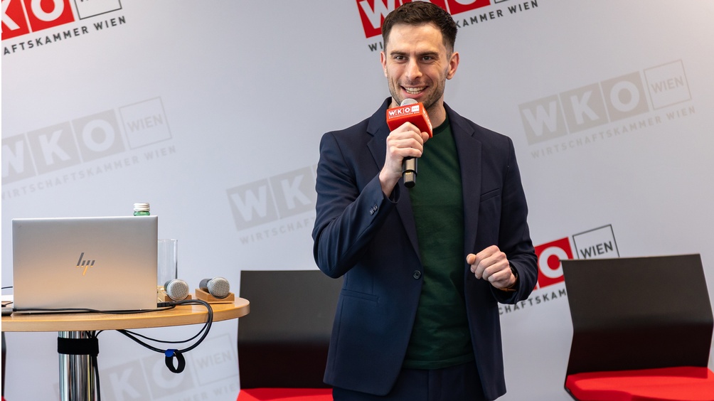 Lächelnde Person steht auf einer Bühne und spricht in ein Mikrofon