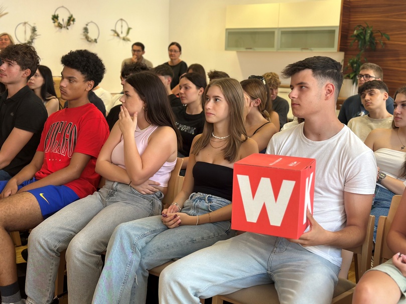 Eine Gruppe von Schülern sitzt auf Stühlen und hört bei einem Vortrag zu