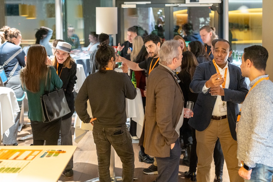 Menschen bei einer Veranstaltung, die sich unterhalten. Sie stehen an runden Tischen. 
