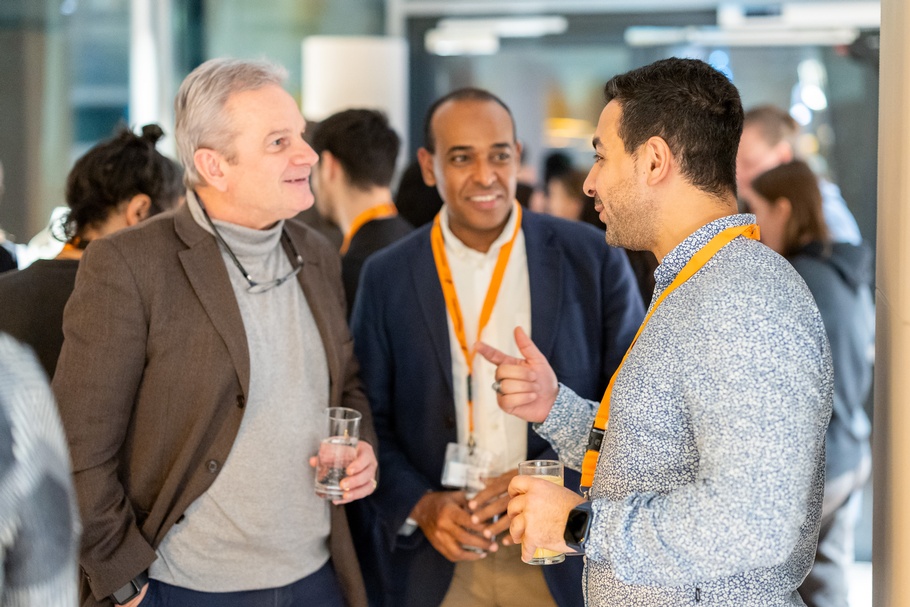 Zu sehen sind Personen bei einem Event, die sich unterhalten und Gläser mit Flüssigkeiten in der Hand halten.