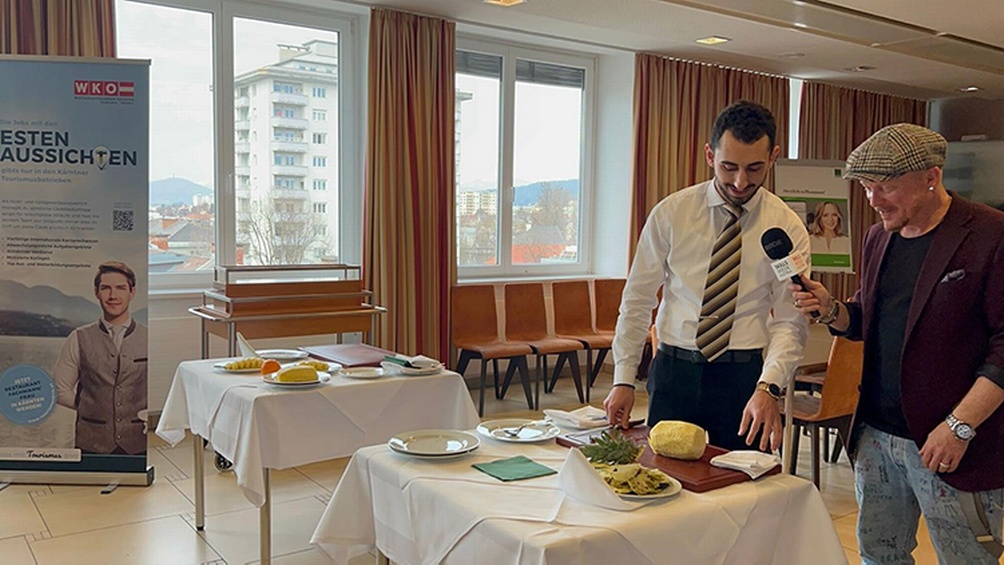 Person mit Mikrofon interviewt weitere Person vor gedecktem Tisch