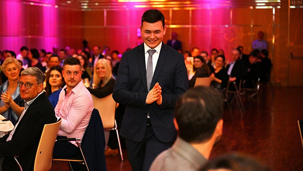 Lächelnde Person geht durch violettpink erleuchteten Festssal mit applaudierendem Publikum