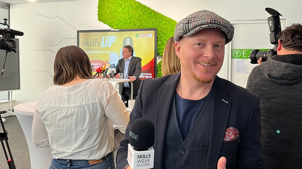 Person mit Kappe und Mikrofon in der Hand steht vor Rednerpodest