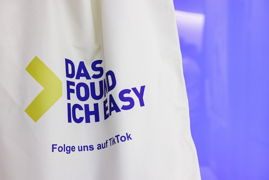 Naufnahme einer weißen Jutetasche vor violett-floriszierendem Hintergrund. Auf der Tasche steht der Schriftzug Das found ich easy Folge uns auf TikTok