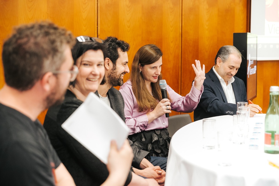 Frau mit Mikrofon und vier weitere Teilnehmer:innen an einem Tisch