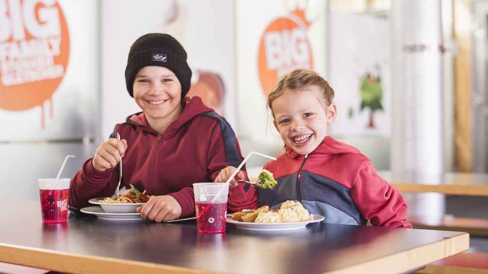 Zwei junge Personen mit Speeisen und einem Getränk vor sich an einem Tisch sitzend