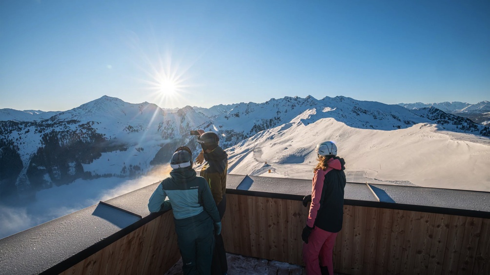 Drei Personen betrachten auf einer Terrasse stehend die Berge