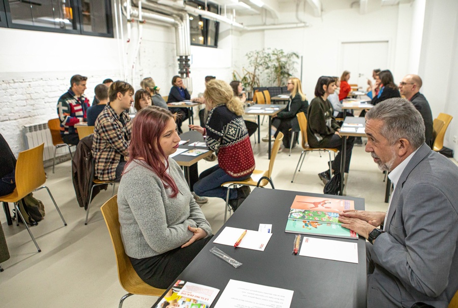 Eine Gruppe von Erwachsenen sitzt an Schreibtischen und führt Gespräche