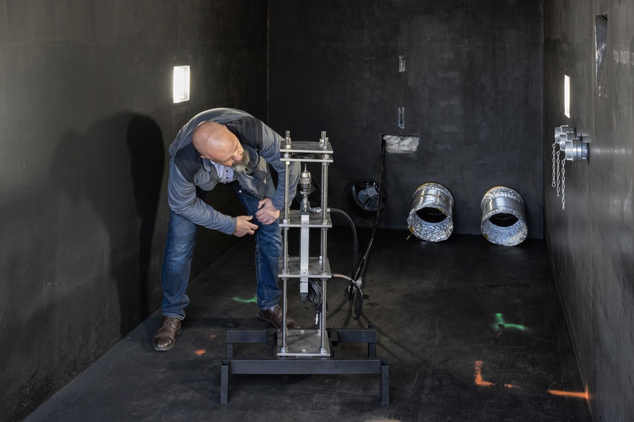 Schwarze Testkammer, eine bärtige Person begutachtet eine Batterie