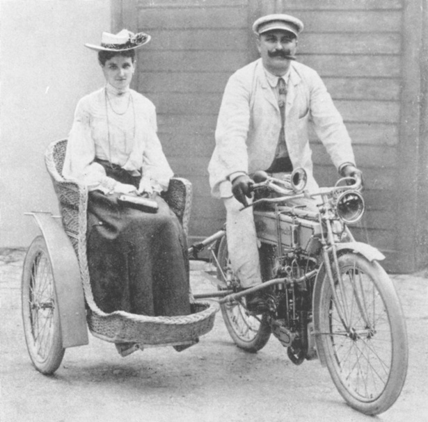 Ein Frau und ein Mann fahren auf einem Puch-Motorrad mit Beiwagen. Bild ist aus 1900.