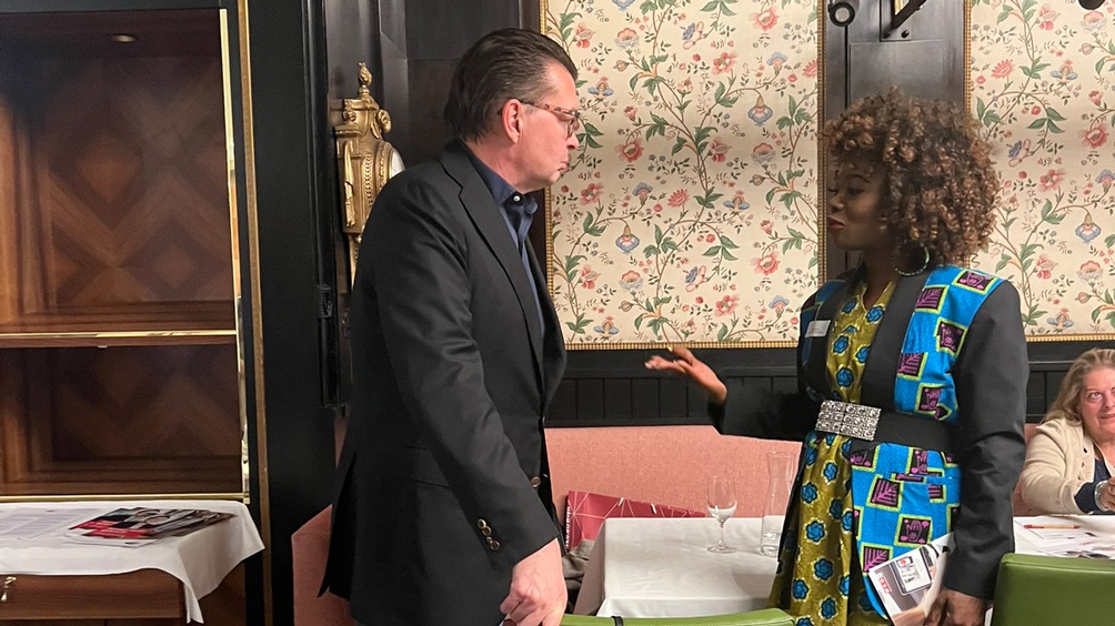 Seitenansicht zweier Personen im Gespräch miteinander, im Hintergrund floral gemusterte Tapete und Holzvertäfelung