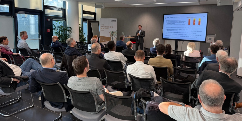 Personen sitzen während einer Veranstaltung im Publikum und hören zu.