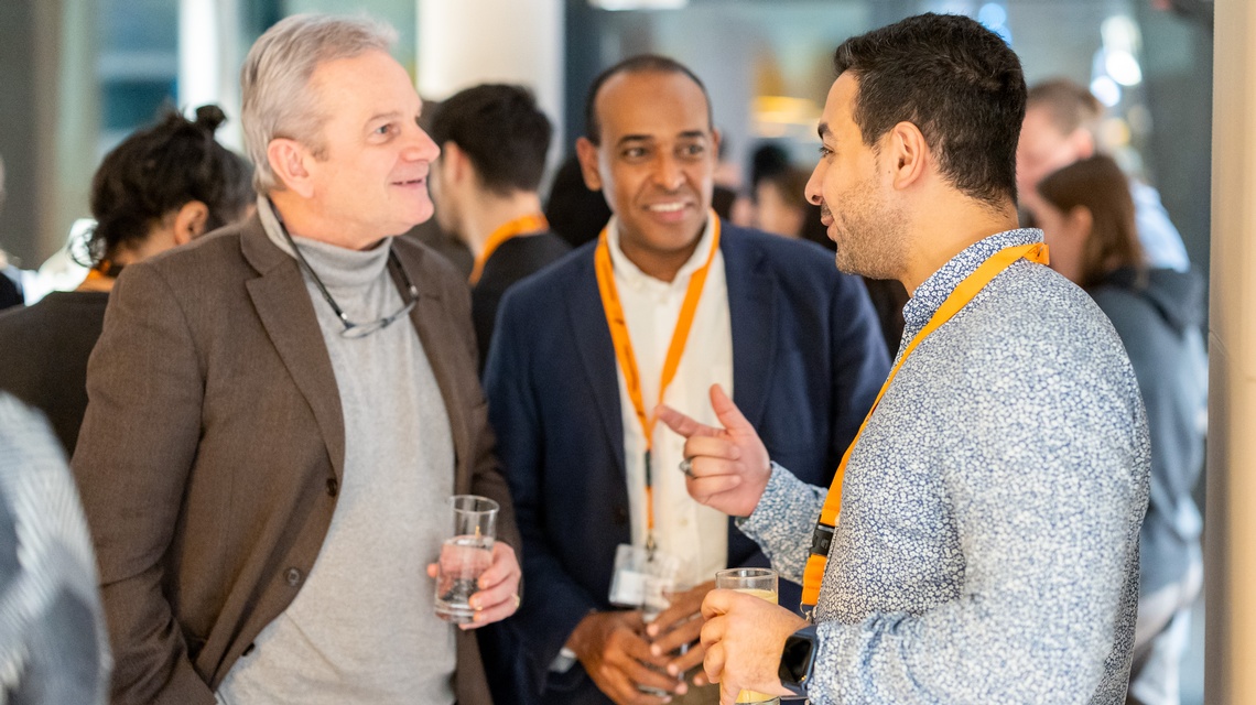 Zu sehen sind Personen bei einem Event, die sich unterhalten und Gläser mit Flüssigkeiten in der Hand halten.