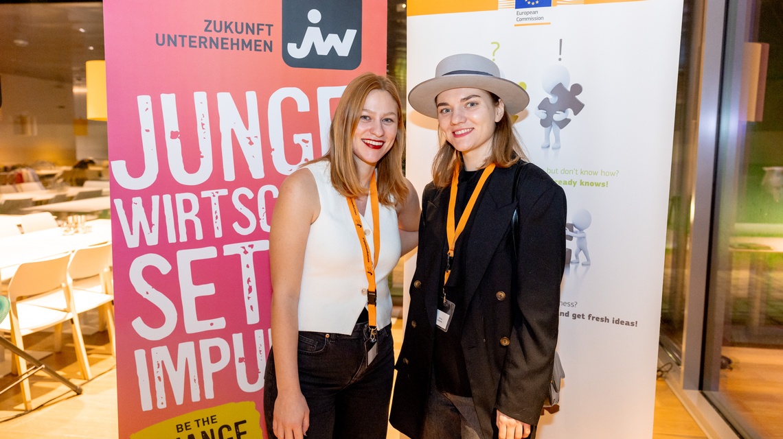 Zu sehen sind zwei Personen, die vor einem Roll-up stehen. Auf dieses ist 