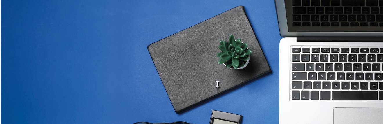 Laptop, Notizbücher, Taschenrechner, Brille sowie Stift, Büroklammer liegen auf einem blauen Untergrund, Topshot