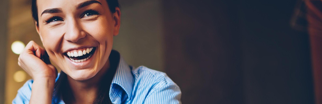 Lachende Person in blaugestreiftem Hemd stützt einen Arm an die Wange, der andere Arm am Tisch abgestützt mit iWatch am Handgelenk