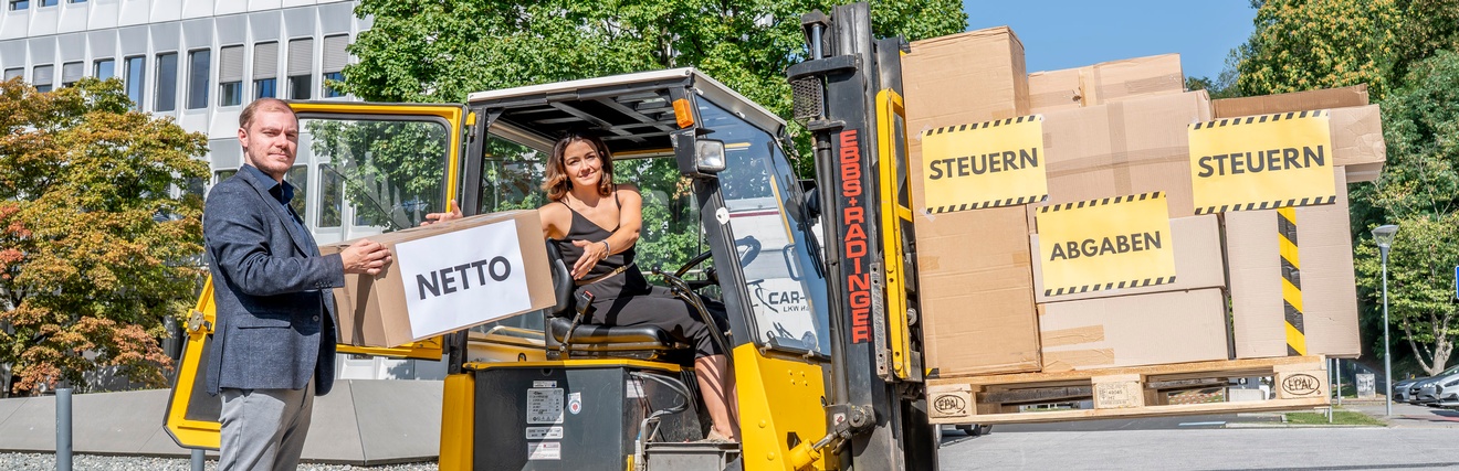 Hella Riedl-Rabensteiner, Vorsitzende der Jungen Industrie Steiermark, sitzt auf einem Gabelstapler, Christian Wipfler, Landesvorsitzender der Jungen Wirtschaft, überreicht ihr ein Paket auf dem Netto geschrieben steht