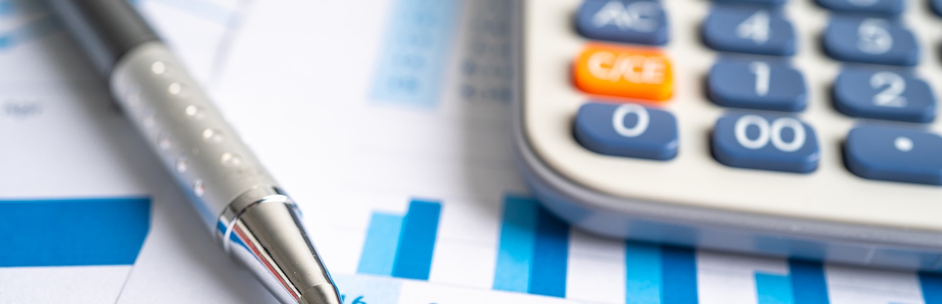 Detailansicht eines Blattes mit eines Zahlen und statistischem Diagramm, darauf deutend Spitze eines Kugelschreibers und Taschenrechner darauf liegend im Ausschnitt