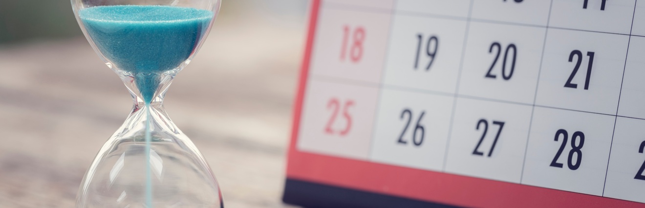 Eine Sanduhr mit blauem Sand sowie ein Kalender stehen auf einem Holztisch