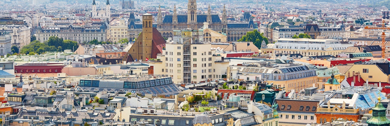 Panoramaaufnahme Teile der Stadt Wiens mit verschiedenen Sehenswürdigkeiten im Vordergrund. Im Hintergrund sind weitere Gebäude und Hügel