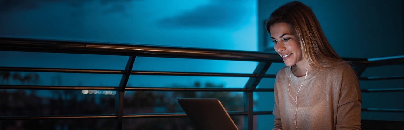 Eine junge Frau am Laptop auf einer Dachterrasse. Blaue Dämmerung im Hintergrund.