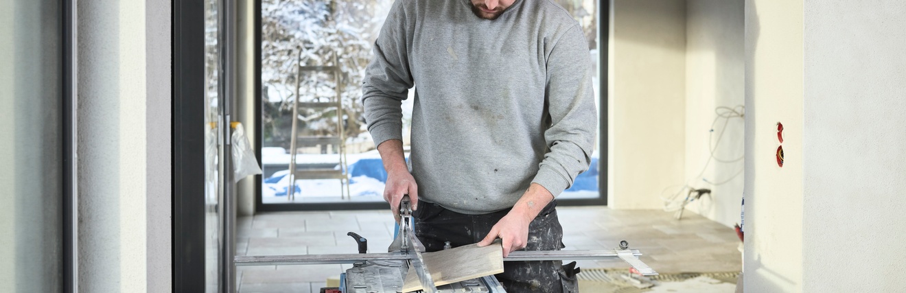 Ein Mann schneidet eine graue Fliese an einem Fliesenschneidegerät. 