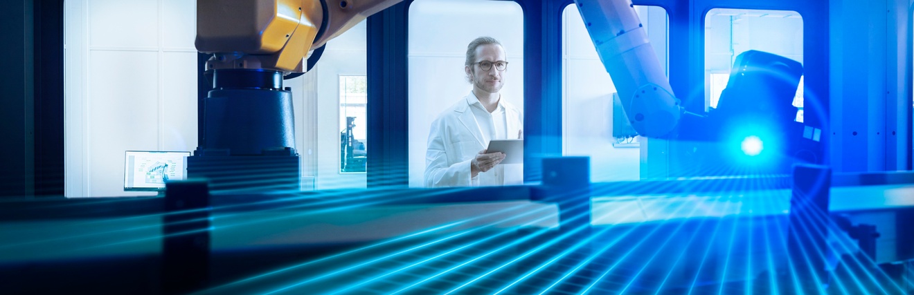 Person mit Brillen und in weißem Laborkittel blickt durch Glasscheibe auf Roboterarm mit blauem Laserlicht