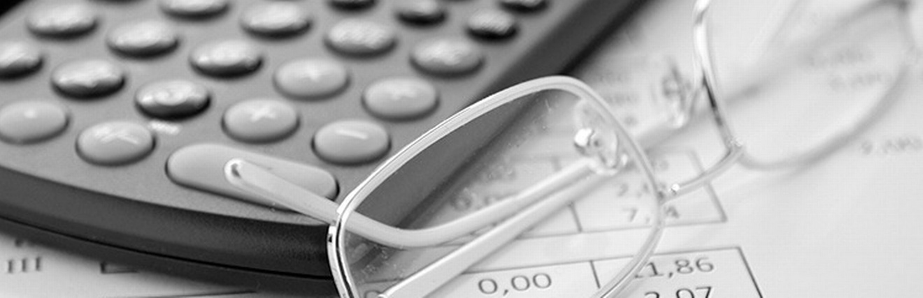 Detailansicht Brille neben Taschenrechner auf Papier mit Zahlen liegend