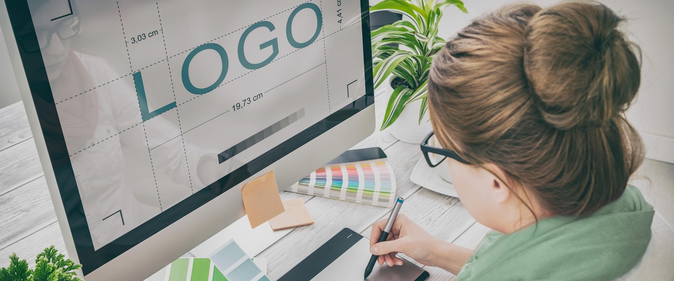 Person sitzt vor einem PC und zeichnet ein Logo während sie eine Farbkarte in der Hand hält