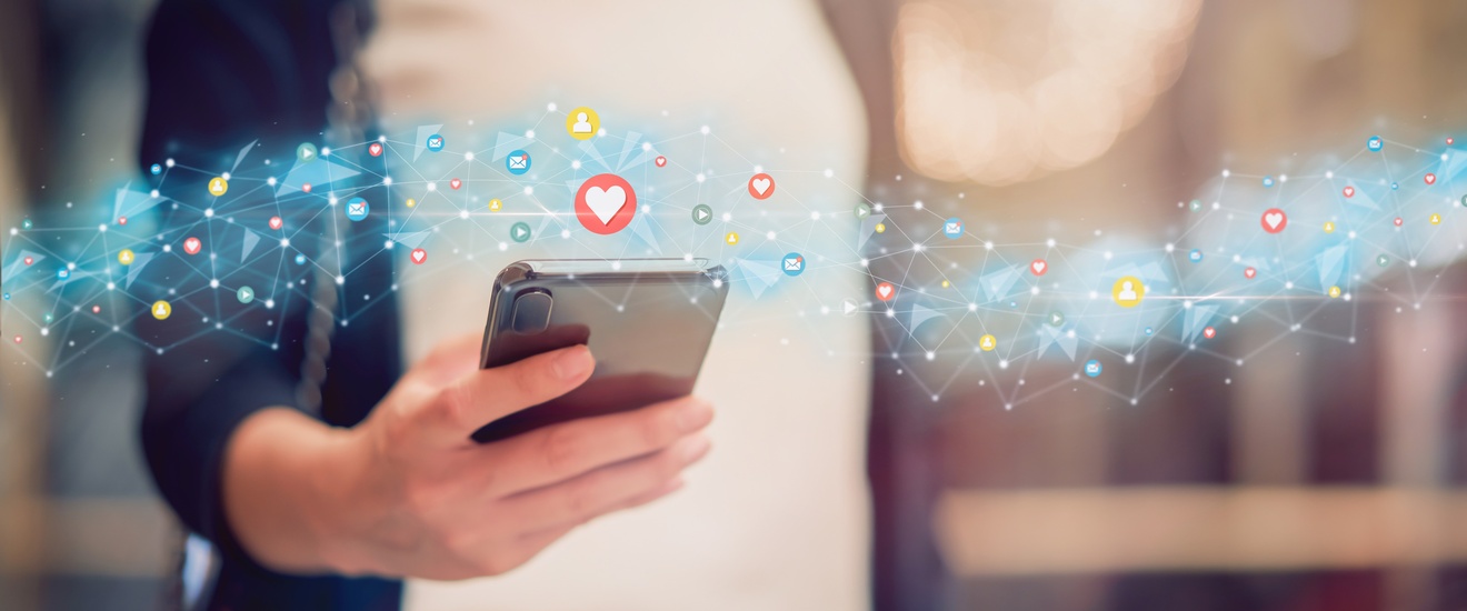 Detailansicht einer Hand, die Smartphone hält, darüberliegend Overlay von leuchtenden Linien und Social-Media-Icons