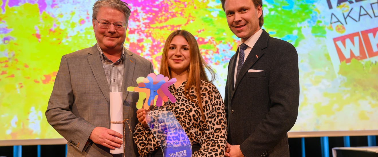 zwei Männer und eine junge Frau posieren für das Foto, sie hält einen bunten Pokal in der Hand