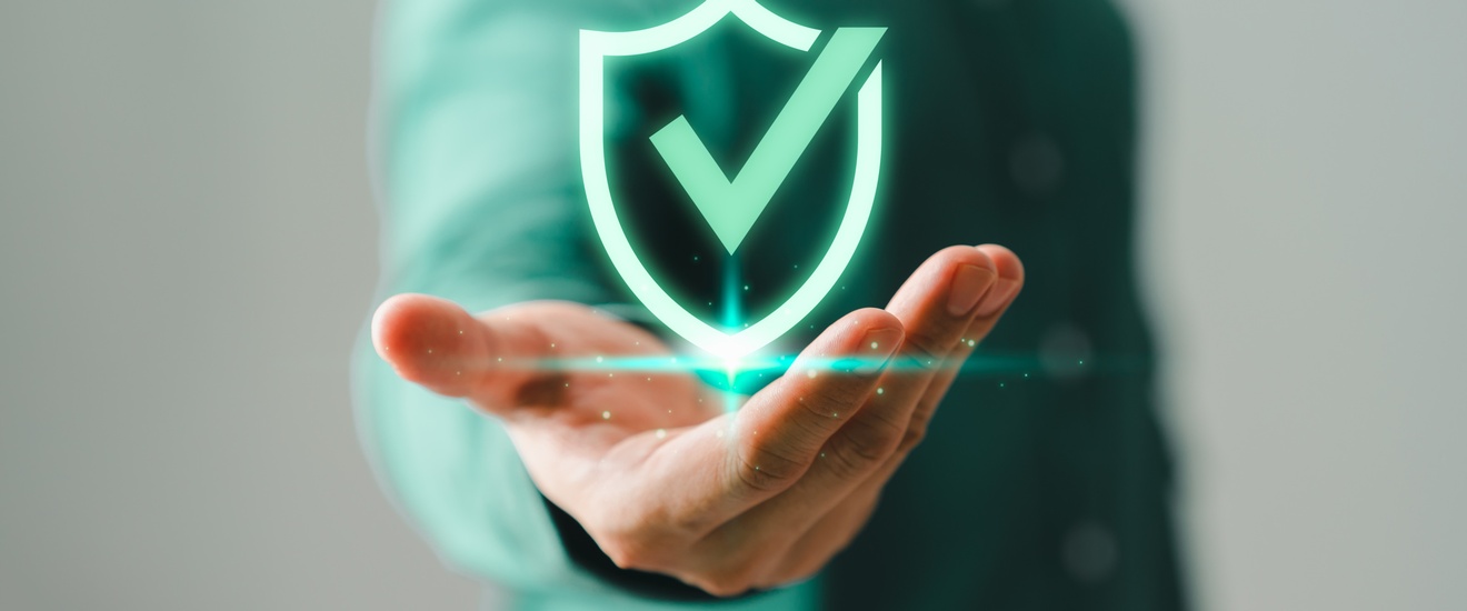 Im Vordergrund ist die Grafik eines grünen Hakens. Darunter ist die Hand einer Person