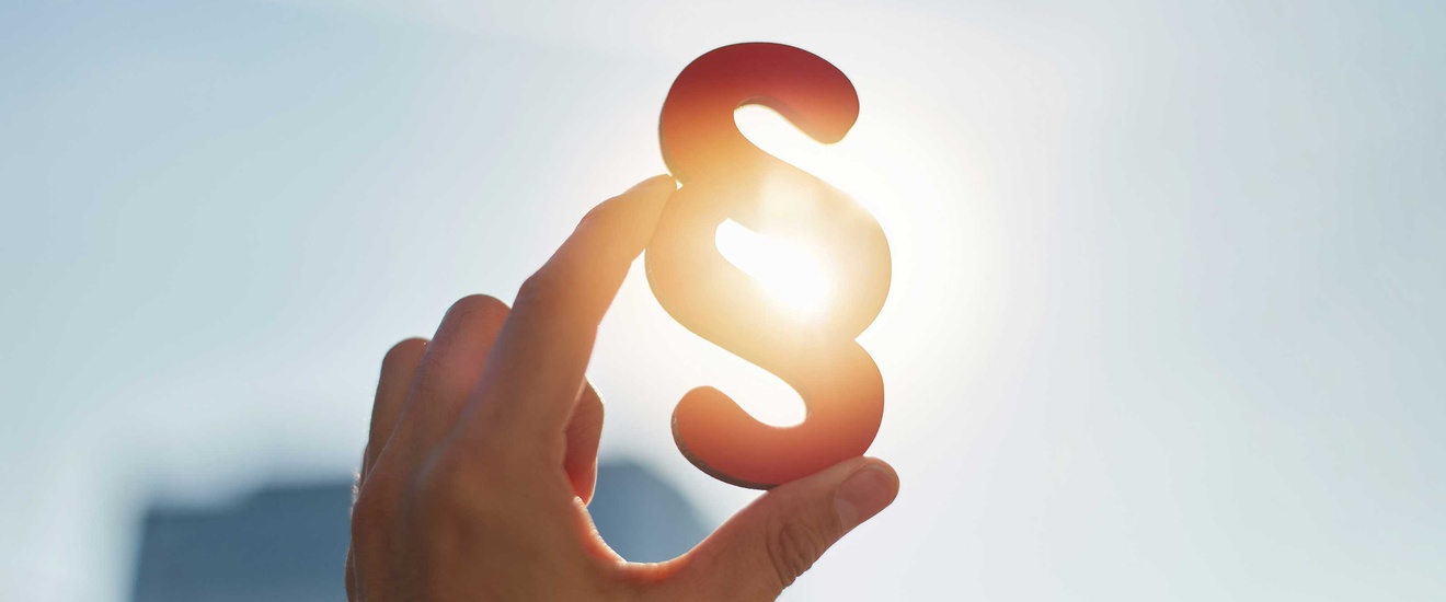 Hand hält Paragraphen Symbol in Sonne 