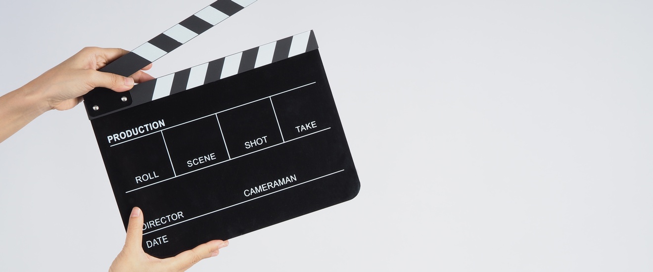 Hände halten eine Filmklappe vor einem hellen Hintergrund