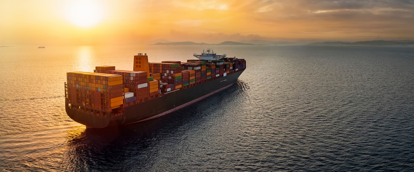 Ein Frachtschiff mit vielen Container fährt auf dem Meer. Im Hintergrund ist Festland