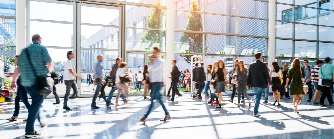 Personen gehen durch eine helle Eingangshalle aus Glas