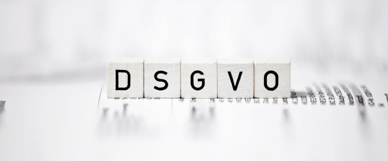 Weiße Würfel mit dem Aufdruck DSGVO, die auf einem textlichen Papier aufliegen und ringsum zeigt sich Unschärfe