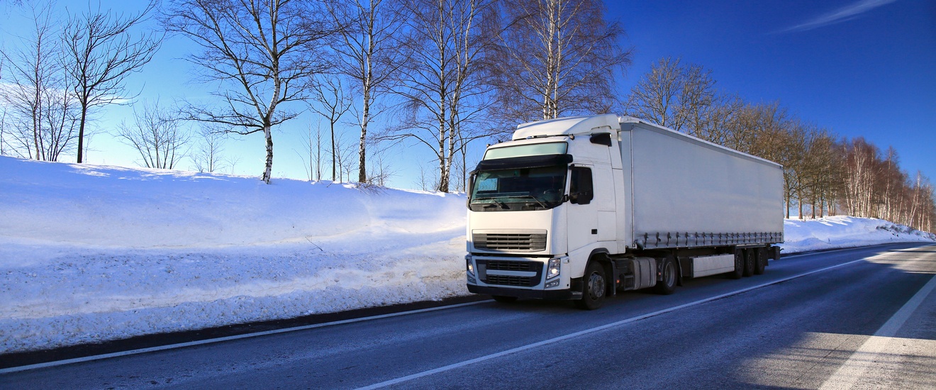 Weißer LKW fährt entlang einer Straße mit Winterlandschaft und Schnee