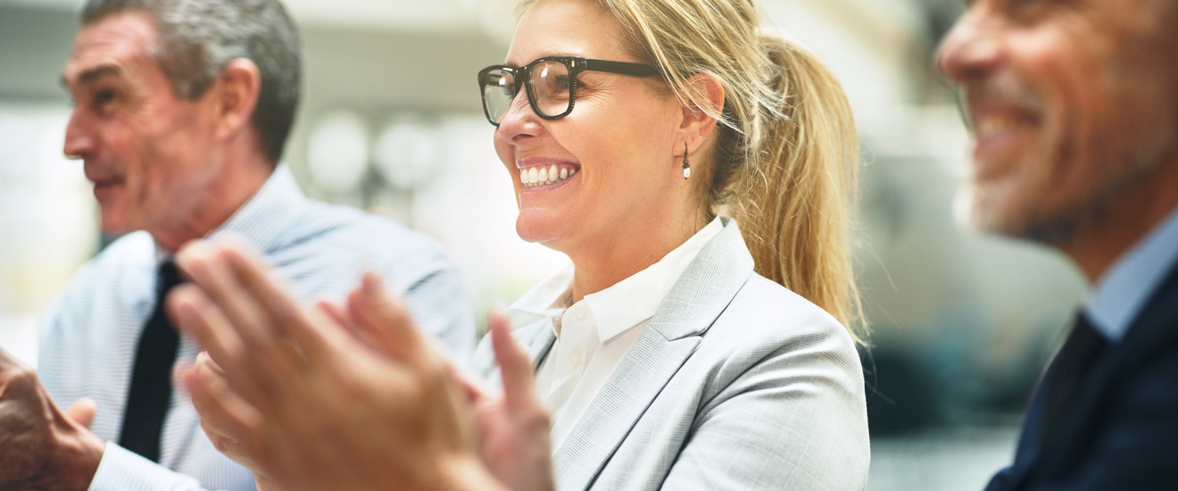 Drei Personen in Businesskleidung sitzen nebeneinander und applaudieren.