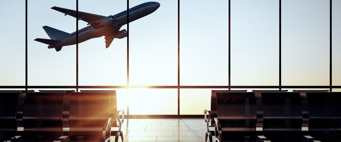 Ein moderner, leerer Flugsteig bei großen Glasfenstern, aus denen man bei Sonneneinstrahlung ein sich im Steigflug befindliches Flugzeug beobachten kann.