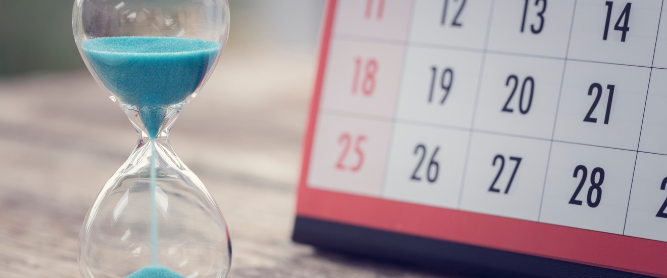 Eine Sanduhr mit blauem Sand sowie ein Kalender stehen auf einem Holztisch