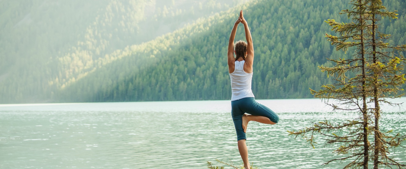 Person in Yogapose vor See mit Waldlandschaft