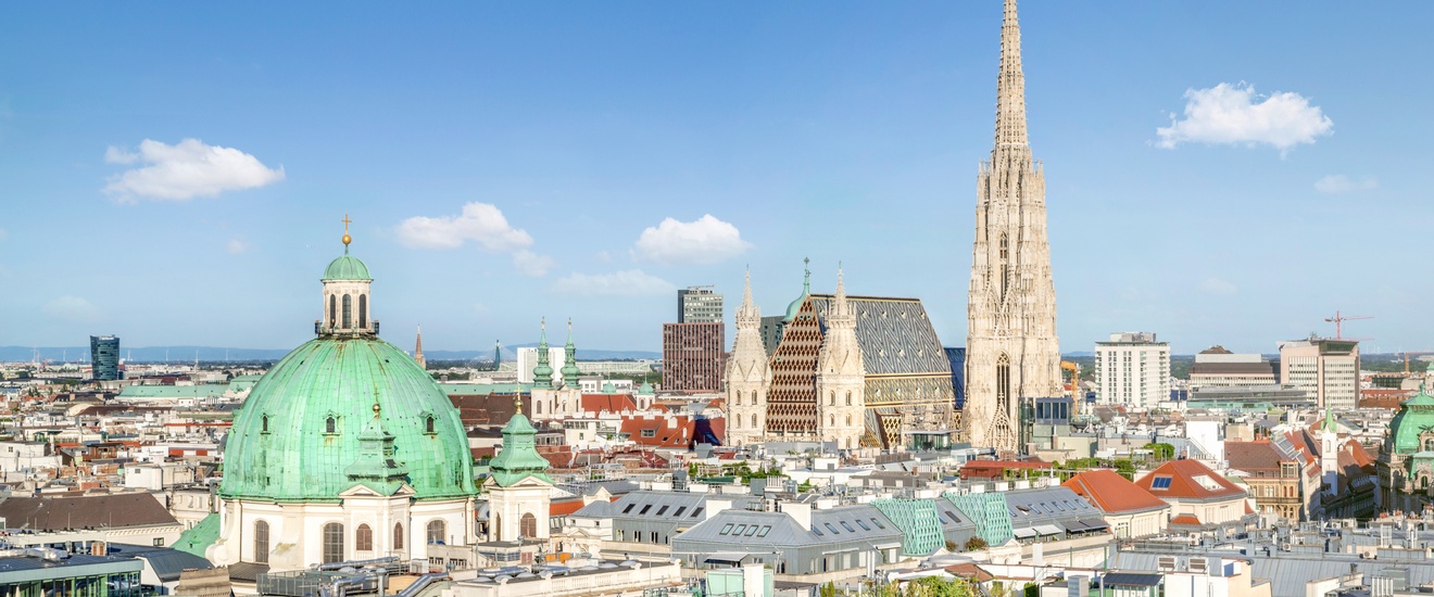 Blick von oben auf die Häuserlandschaft des ersten Wiener Bezirks, im Vordergrund die grüne Kuppel der Peterskirche, im Hintergrund der Stephansdom