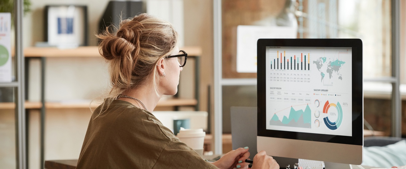 Person mit Brillen sitzt vor Computermonitor mit Diagrammen
