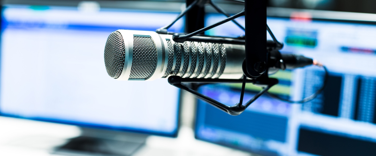 Nahaufnahme eines Mikrofons in einer Nachrichtenstation, im Hintergrund stehen zwei große Monitorbildschirme
