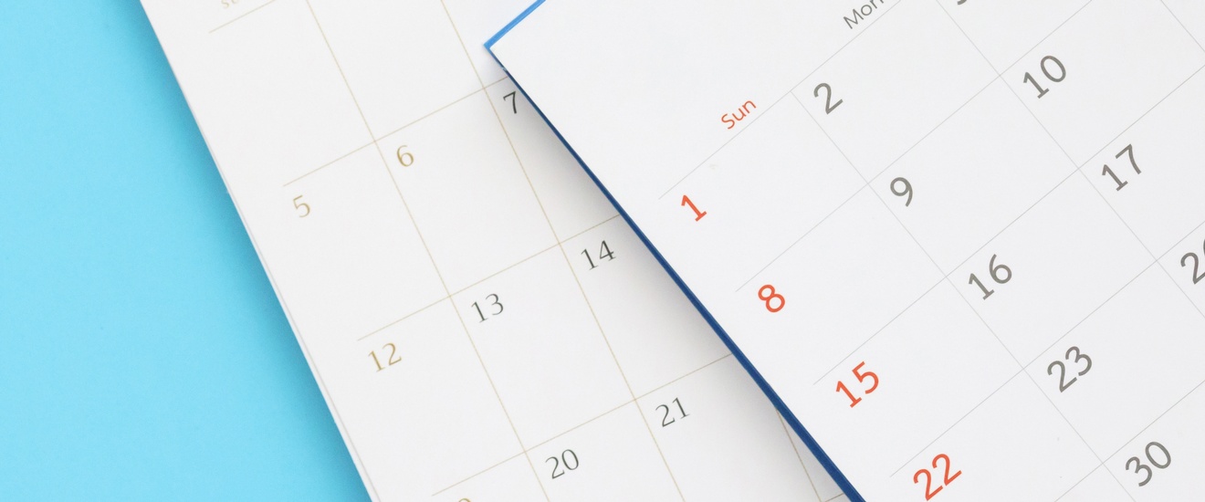 Nahaufnahme zweier übereinander, leicht versetz, liegender Ausschnitte von Kalenderblättern vor blauem Hintergrund