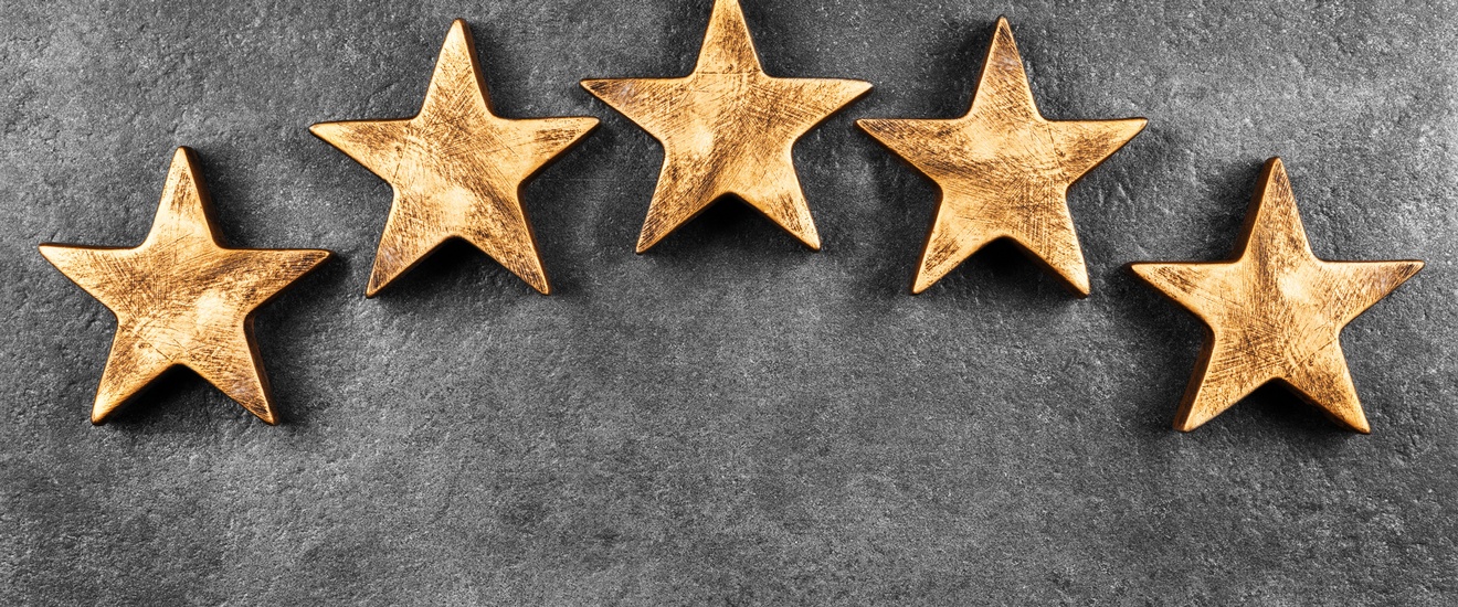 Fünf goldene Sterne liegen zu einem Halbkreis drapiert auf einem grauen Untergrund